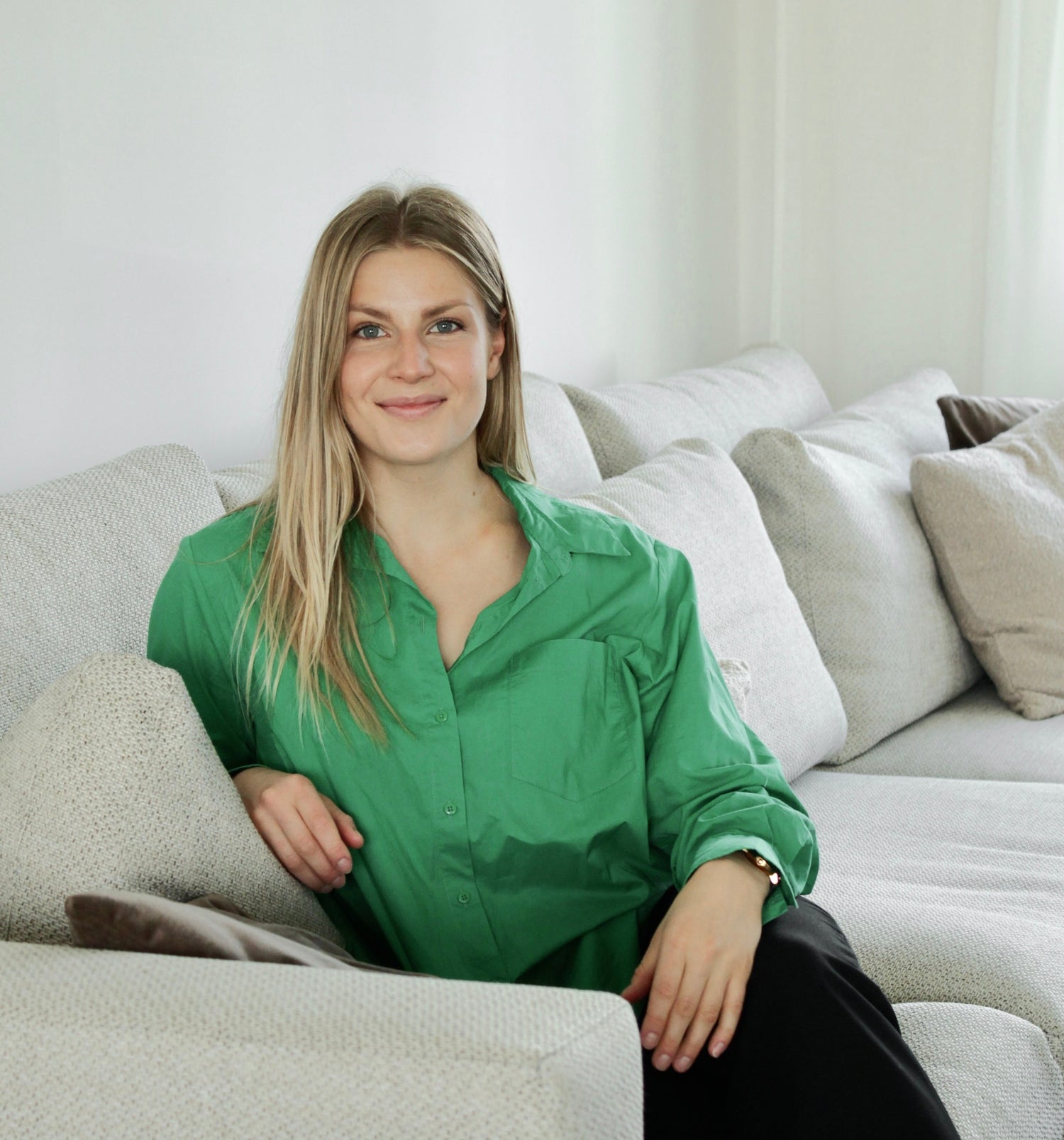 Woman in a green shirt sitting on a white couch in a minimalistic room.